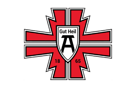 Logo mit rotem Kreuz, schwarzem Schild und der Aufschrift „Gut Heil“ sowie der Jahreszahl „1865“.