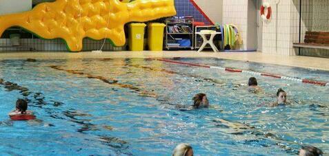 Schwimmerinnen genießen das Wasserspiel in einem Hallenbad mit einer gelben Riesenrutsche im Hintergrund.